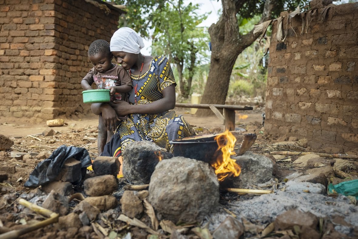 Ugandalainen Catherine valmistaa ruokaa lapsi sylissään.