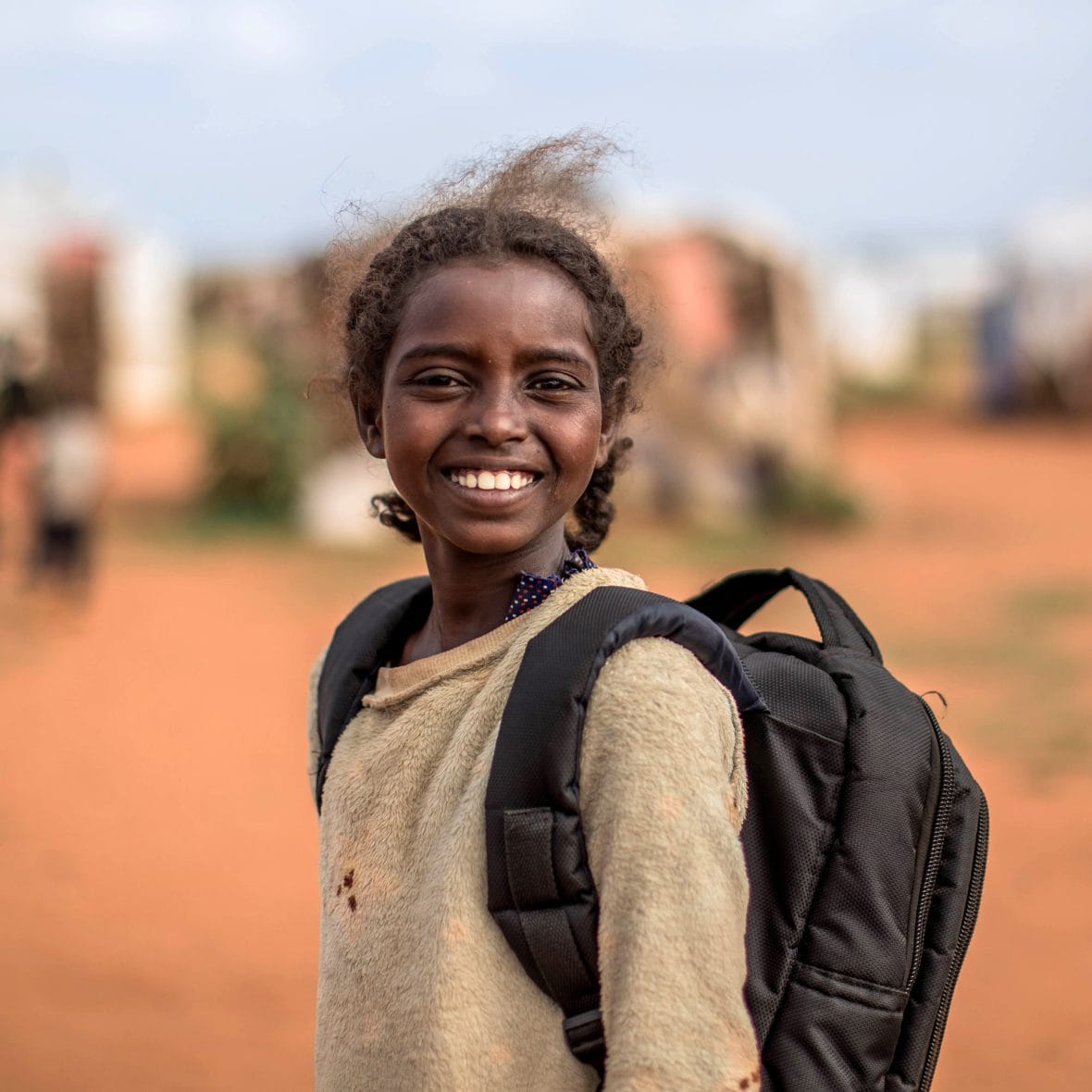 Tyttö hymyilee koulureppu selässä.
