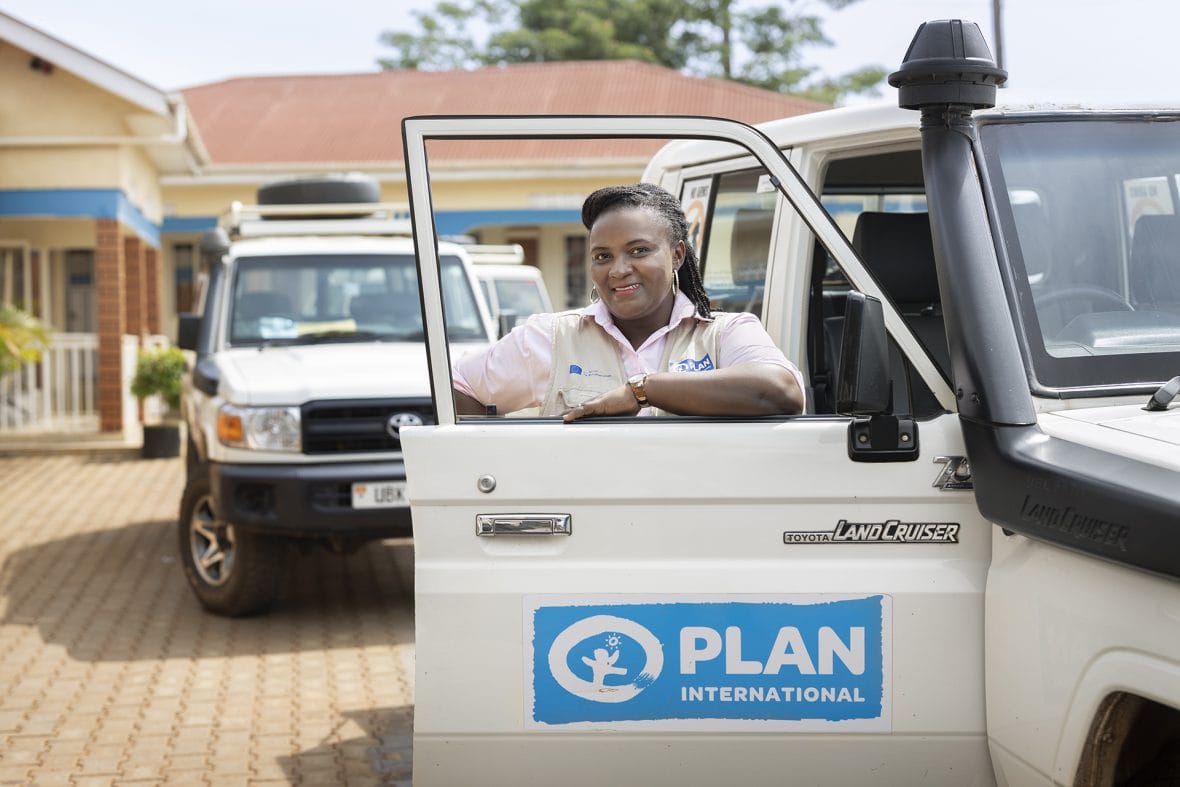 Planin työntekijä Christine Oseku istuu autossa, jonka ovessa on iso Planin logo.