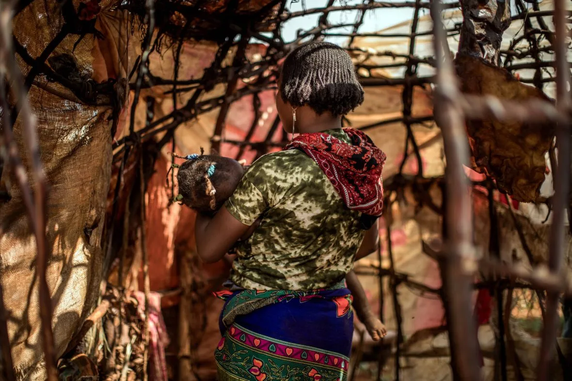 Nuori äiti pitää lasta sylissään ja on selin kameraan.