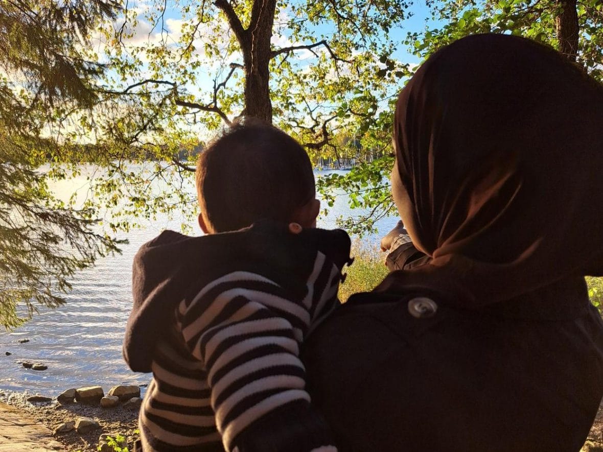 Äiti pitää lastaan sylissä ja katsoo syksyistä järvimaisemaa.