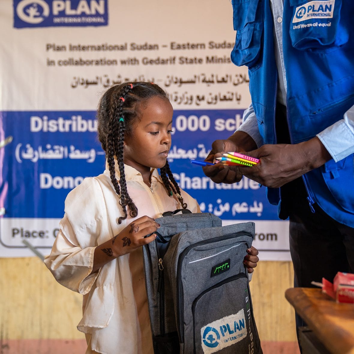 Planin työntekijä ojentaa nuorelle tytölle koulurepun sekä koulutarvikkeita.