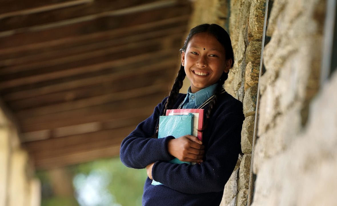 Koulutyttö nojaa seinään. Hänellä on sylissään koulukirjoja.