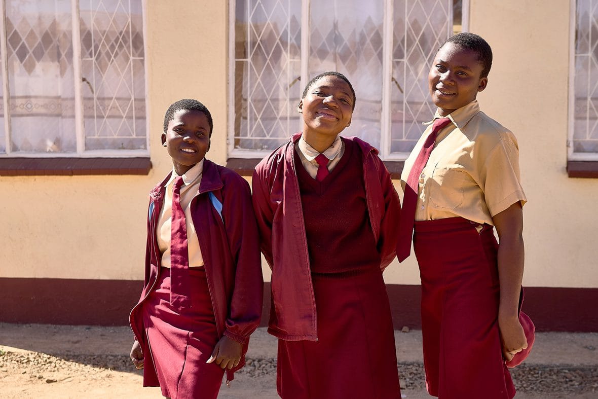 Kolme koulutyttöä Zimbabwessa koulun pihalla kouluasuihin pukeutuneina.