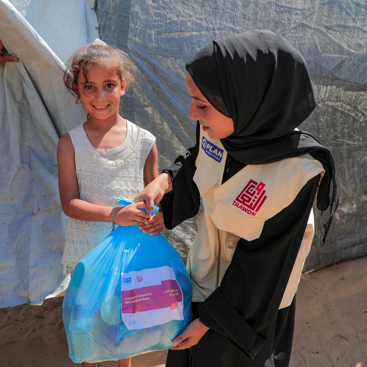 Planin kumppanijärjestön työntekijä antaa ruoka-apupaketin lapselle pakolaisleirillä Gazassa.
