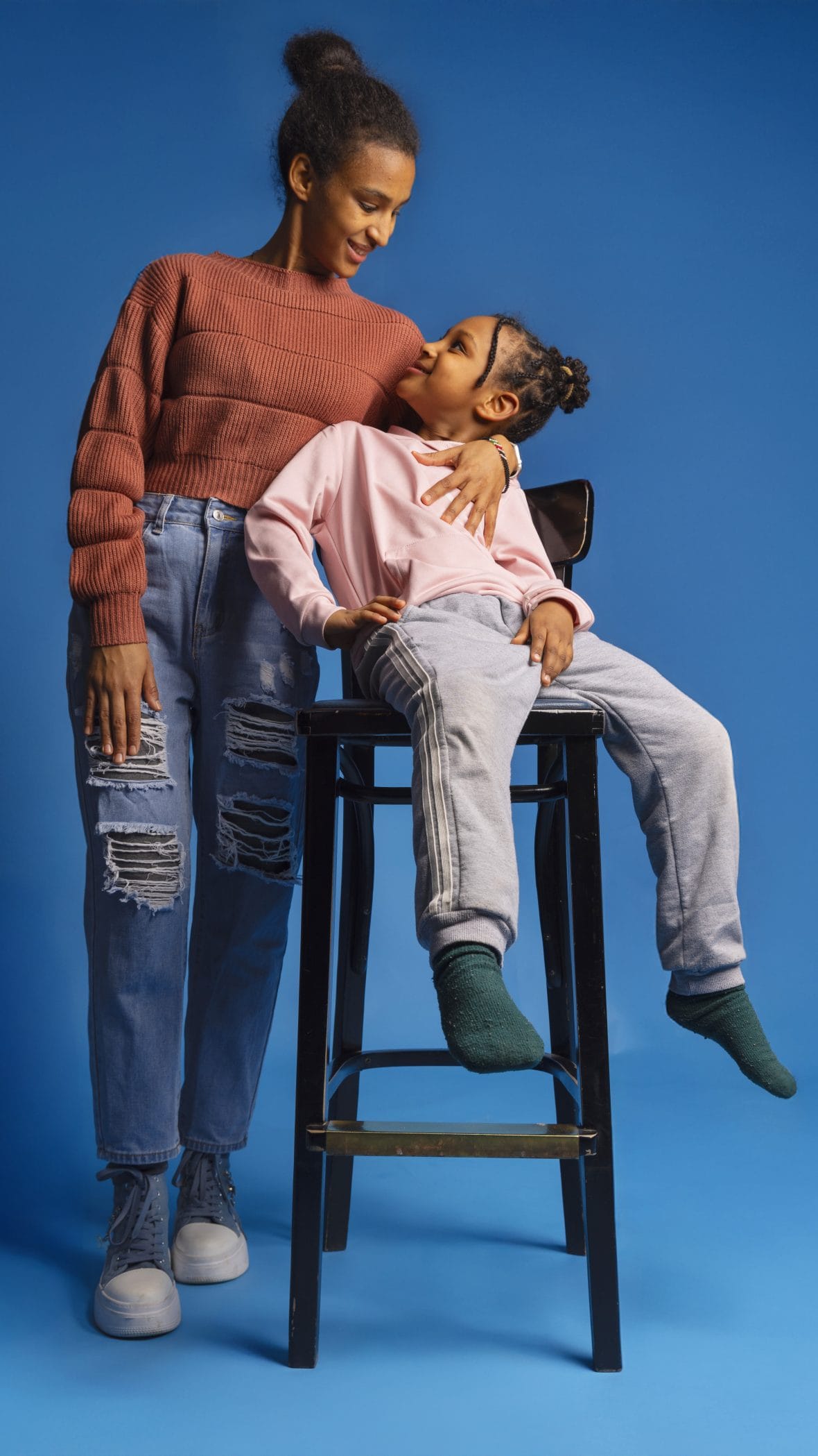 Osaava nuori äiti -hankkeen äiti ja lapsi katsovat toisiaan hymyillen. Tytär istuu korkealla tuolilla ja äiti seisoo vieressä käsi lapsen ympärillä.