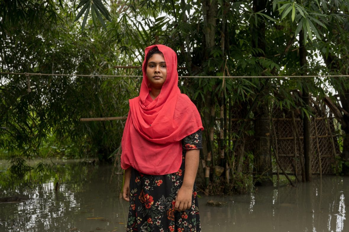 Bangladeshilainen nuori nainen seisoo tulvivan ympäristön keskellä.